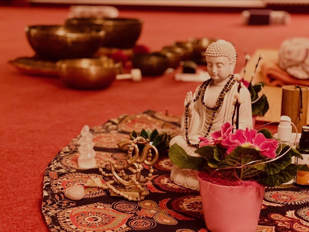 Entspannungstechniken im Überblick: Die wirksamsten Methoden für innere Ruhe 3 Klangschalen, Buddha-Figur und Blumen auf einem Tuch im Kursraum – vorbereitet für eine Klangschalen-Entspannung