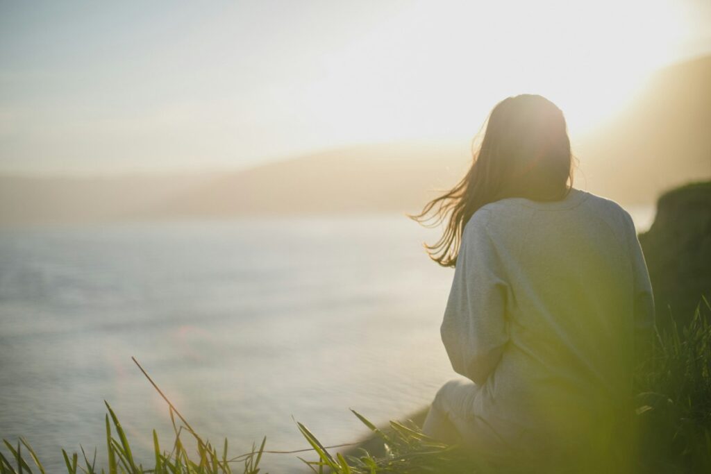 Entspannungstechniken im Überblick: Die wirksamsten Methoden für innere Ruhe 2 Frau sitzt still am Meer im Morgenlicht und übt Meditation und Achtsamkeit